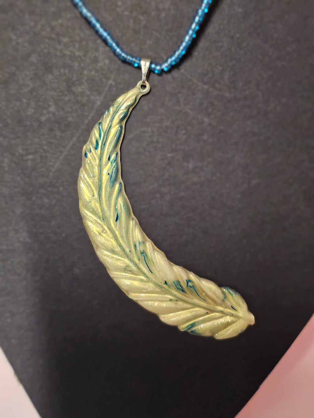 golden feather pendent on blue beaded chain
